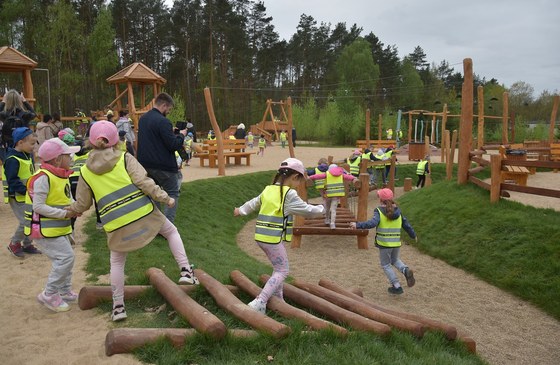 Dzieci w odblaskowych kamizelkach biegające i bawiące się na drewnianym placu zabaw.