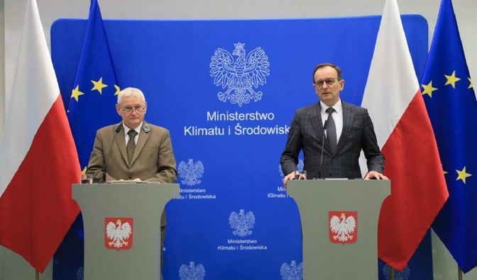 Konferencja w sprawie wykupu gruntów. Przed mównicami stoi dwóch mężczyzn, w tle widać flagi - Polski i Unii Europejskiej/ Fot. Martyna Rychlica
