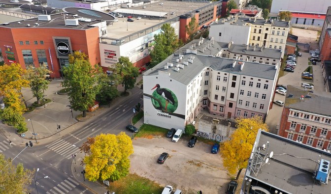 Zdjęcie przedstawia widok z Drona na budynek z muralem oraz jego najbliższe otoczenie.