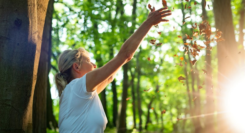 Na zdjęciu widać kobietę w lesie z uniesionymi rękami/ Fot. Tanja Esser/ Shutterstock.com