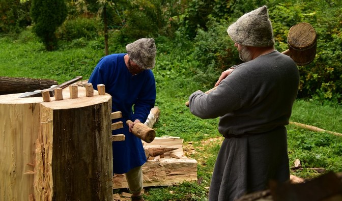 Na fotografii dwóch mężczyzn pobija drewniane kliny do rozłupywania drewna.