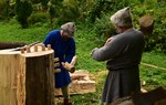 Na fotografii dwóch mężczyzn pobija drewniane kliny do rozłupywania drewna.
