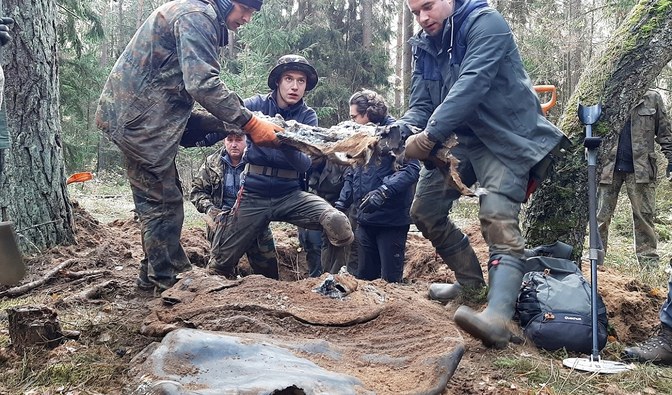 Zdjęcie przedstawia ekipę poszukiwaczy z wydobytym z ziemi fragmentem samolotu