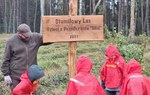 Zdjęcie przedstawia leśnika wraz z dziećmi przy pamiątkowej tablicy o treści "Stumilowy Las Dzieci z Przedszkola "Miś" 2021