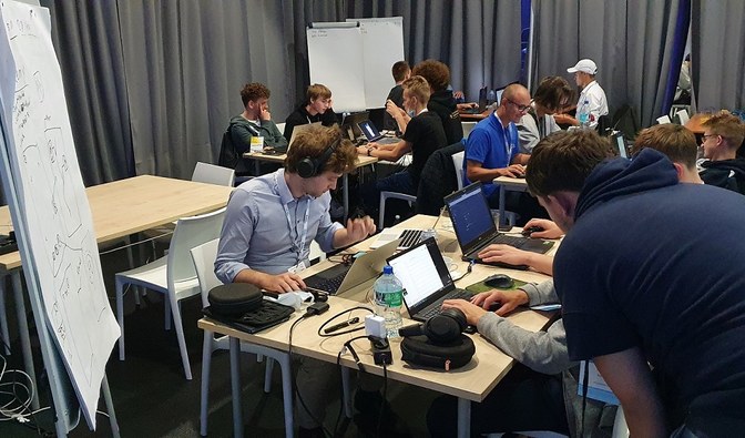 Grupa ludzi siedząca przy stołach i pracująca na laptopach. Fot. Kamil Onoszko
