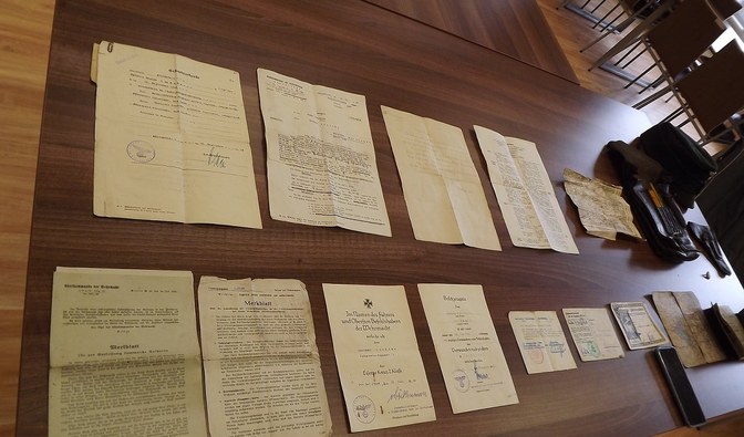Na stole leżą rozłożone dokumenty, pojedyncze kartki, całość pochodzi z czasów drugiej wojny światowej
