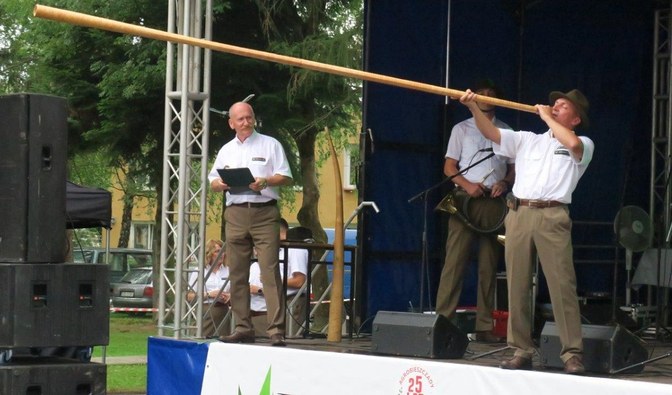Na zdjęciu są widoczne osoby stojące na scenie, jeden z mężczyzn gra na instrumencie muzycznym