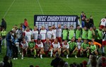 Zdjęcie grupowe obu drużyn piłkarskich, pozujących pod napisem Mecz charytatywny.