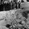 Na czarno-białej fotografii widać rozkopany grób polskich żołnierzy, którzy zostali zastrzeleni w Katyniu; nad grobem stoją mężczyźni w mundurach