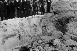 Na czarno-białej fotografii widać rozkopany grób polskich żołnierzy, którzy zostali zastrzeleni w Katyniu; nad grobem stoją mężczyźni w mundurach