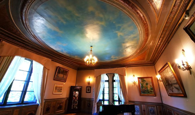 Wnętrze Muzeum Leśnictwa  - Oficyny. W pomieszczeniu z licznymi obrazami na ścianach i sztukaterią na suficie stoi fortepian